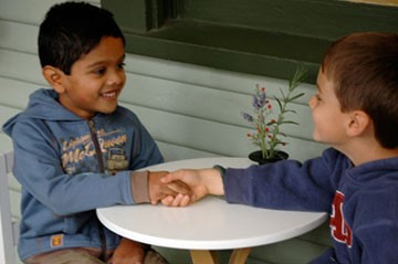 Two children shaking hands across a table, practising grace and courtesy